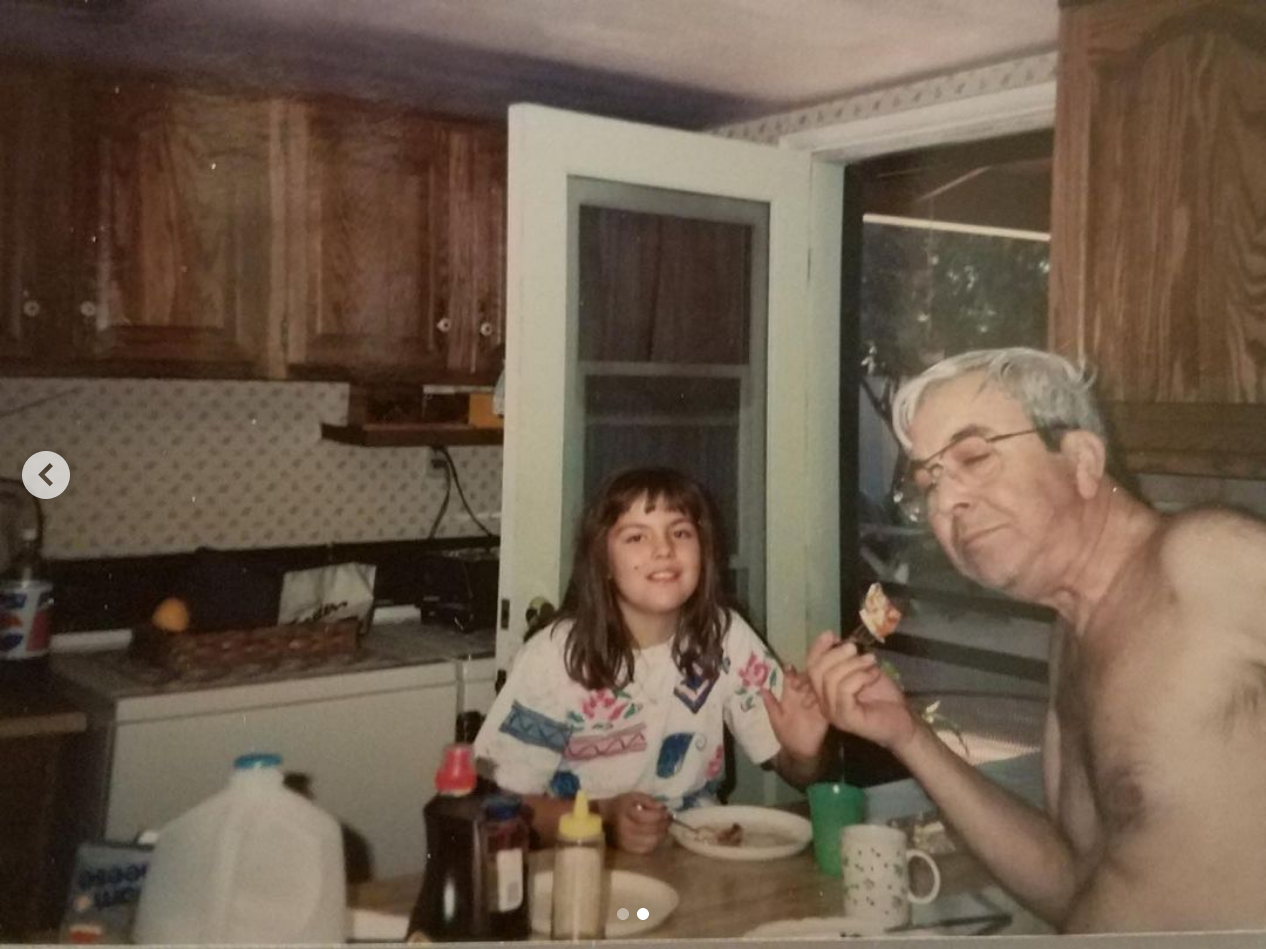 A young girl and her shirtless papu are enjoying pancakes at the breakfast table in the kitchen.